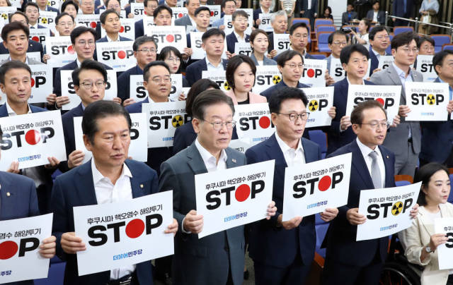2023年8月24日，韓國最大在野黨共同民主黨黨首李在明（前排左二）與議員在首爾國會舉行的緊急會議上手舉標語，抗議日本核污染水排海（新華社）