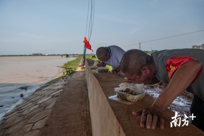 7月9日，江西鄱阳县长江圩堤上，两位值班巡堤村民正在用餐。