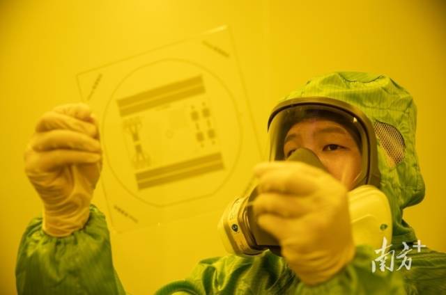 广东欧莱高新材料股份有限公司的薄膜实验室被橙色灯光所笼罩，工作人员正在做光刻实验。