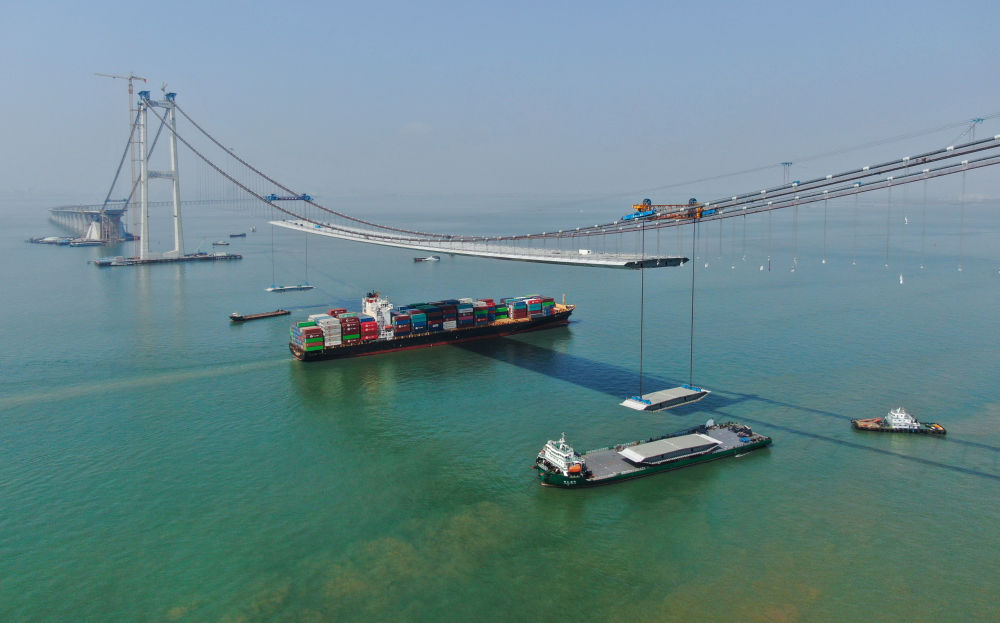 图为2月22日，集装箱货轮通过正在吊装钢箱梁的深中通道伶仃洋大桥（无人机照片）。新华社记者 邓华 摄