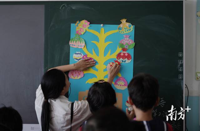 陆婉静正领着孩子们将剪纸作品“石榴树”贴在黑板上。
