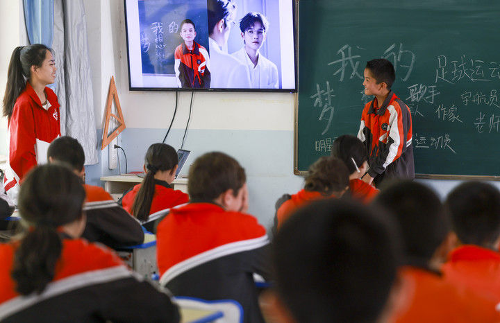 新疆克孜勒苏柯尔克孜自治州阿图什市哈拉峻乡谢依特小学，是一所主要面向柯尔克孜族学生的村级小学，2022年8月成为该州首个西部计划志愿者包校支教的试点学校。23名戍边支教西部计划志愿者服务队的志愿者，在这所小学承担着教书育人的工作。经过近三年的支教服务，学生的学习成绩显著提高，得到当地广泛认可。这是2025年4月23日，支教教师高淑贤（左一）在班级里展示她为学生们制作的“AI梦想职业照”。