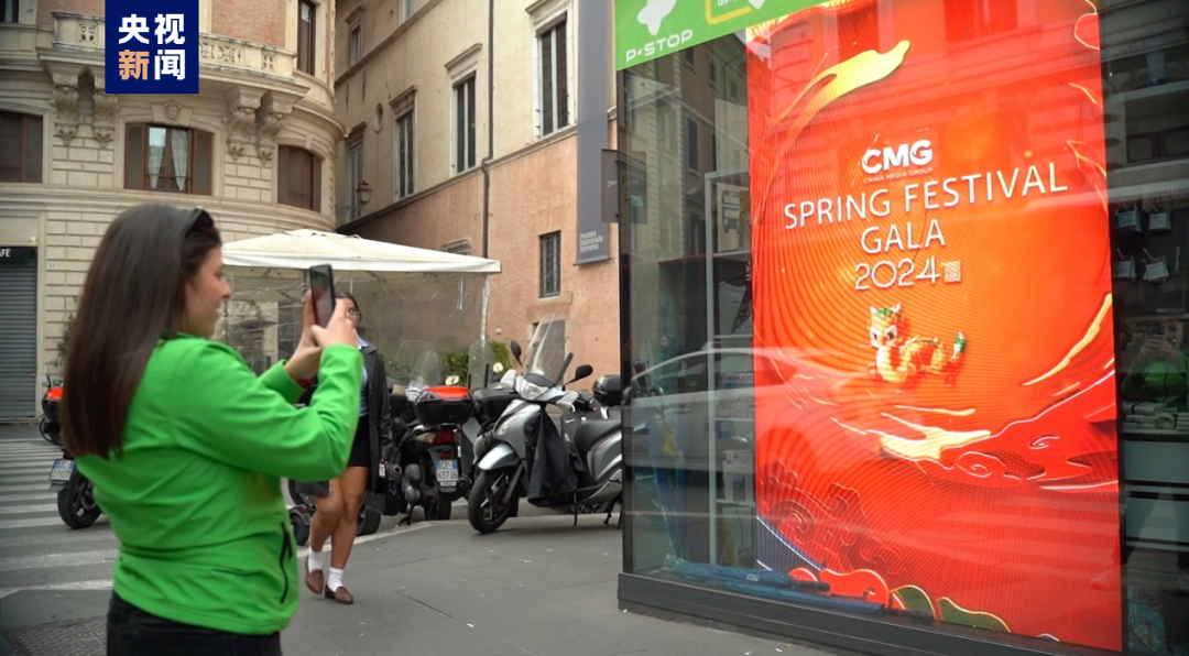 意大利罗马街头，行人在播放总台春晚先导片的屏幕前驻足拍照。