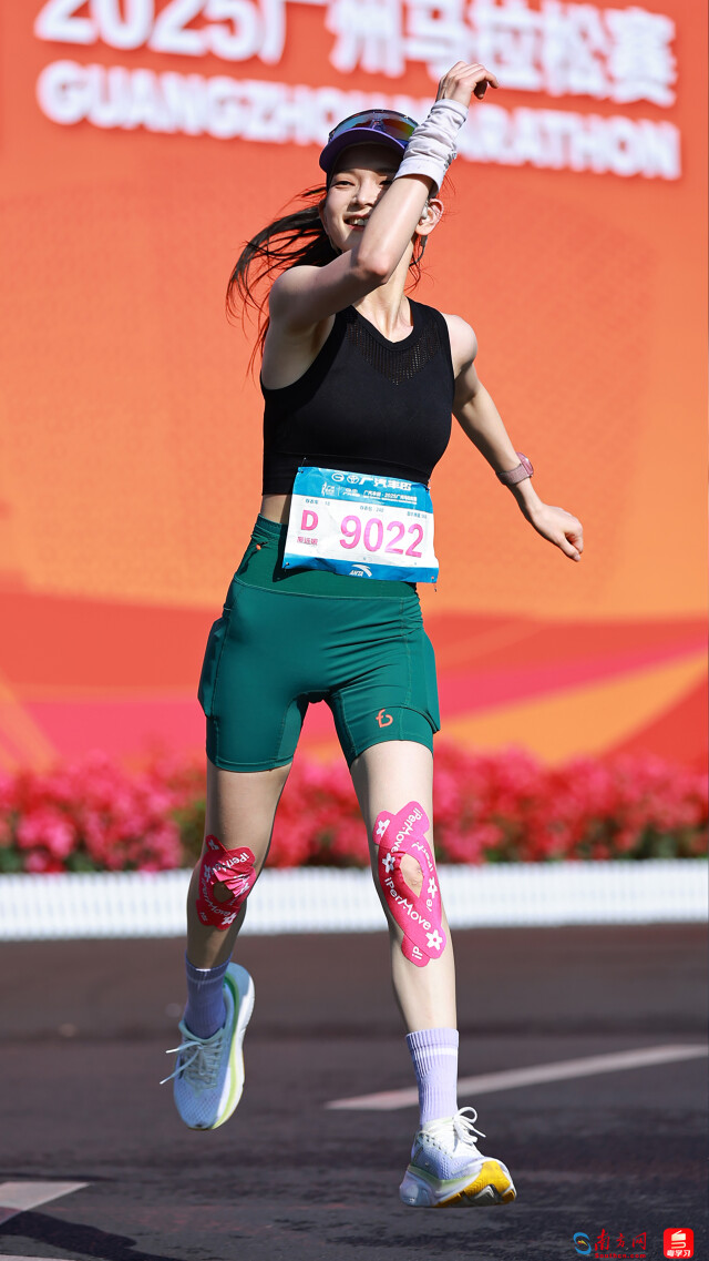2025年12月21日，广州马拉松赛道上，一位女跑者在赛事背景板前跃起欢呼，喜悦与活力展现得淋漓尽致。