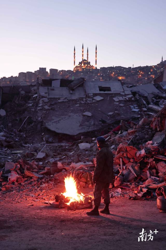 当地时间 2月15日晚，气温骤降，一名土耳其士兵在废墟旁烧火取暖。