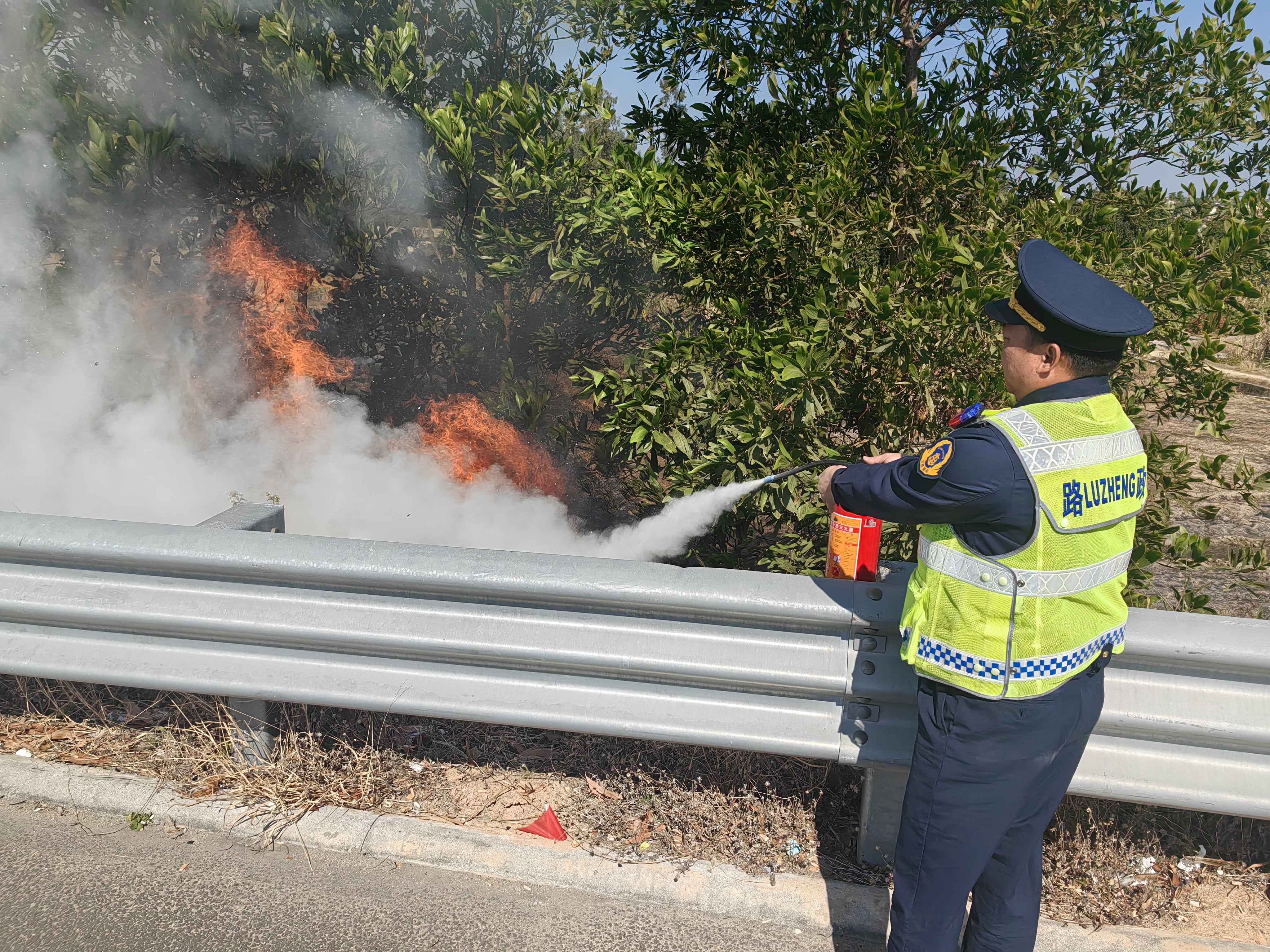 在茂湛高速某边坡,路政队员吴奇建手持灭火器对准护栏外大火喷射。