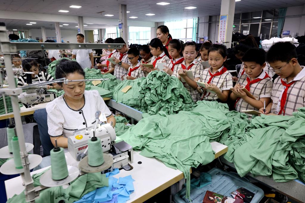 7月28日，在山东省枣庄市税郭镇一家纺织服装企业的成衣车间，参加研学活动的小学生们在了解服装生产过程。新华社发（孙中喆 摄）