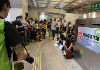 示威者号召到香港税务大楼静坐，仅十余人响应，戴口罩用标语挡脸