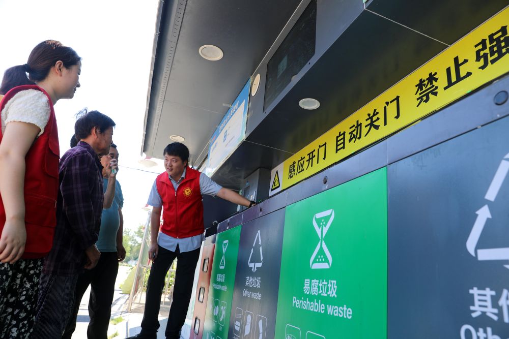 2023年9月1日,志愿者在安徽省合肥市长丰县庄墓镇枣林社区指导居民使用智能垃圾分类回收设备。