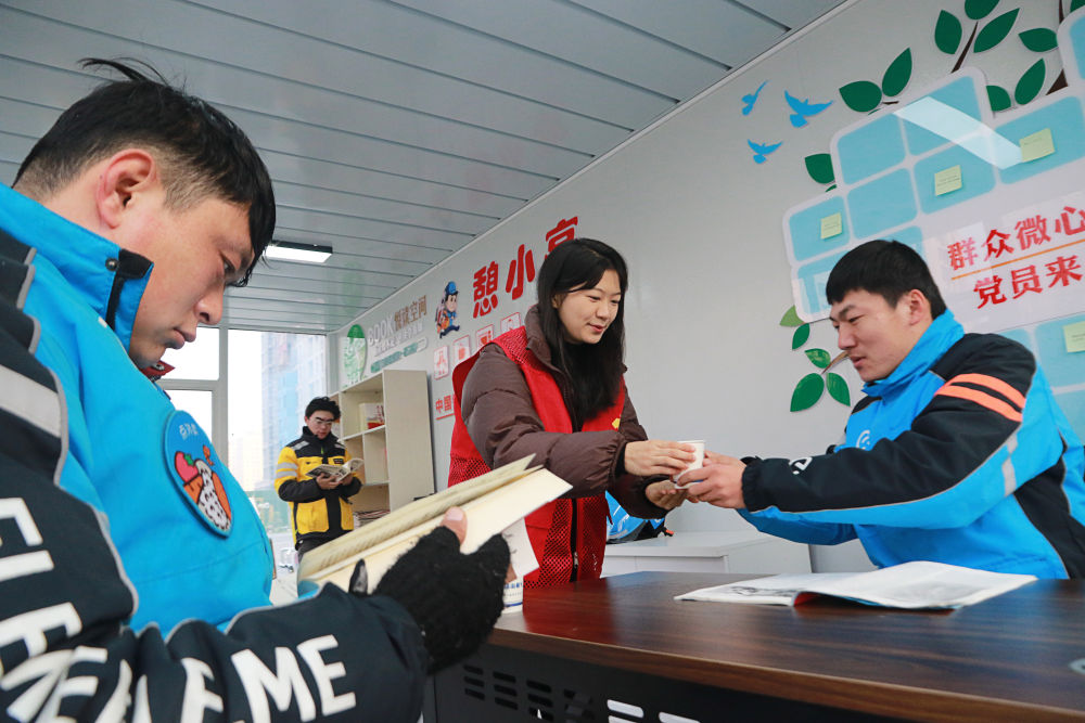 2023年12月27日,志愿者在山东省高密市密水街道“憩小亭”服务站为外卖骑手送上热水。入冬以来,山东省高密市密水街道推进“憩小亭”暖心服务站建设,为外卖骑手、快递小哥、网约车司机、环卫工人等户外劳动者提供饮水、无线上网、食物加热等多项服务,让他们感受到冬日里的温暖。