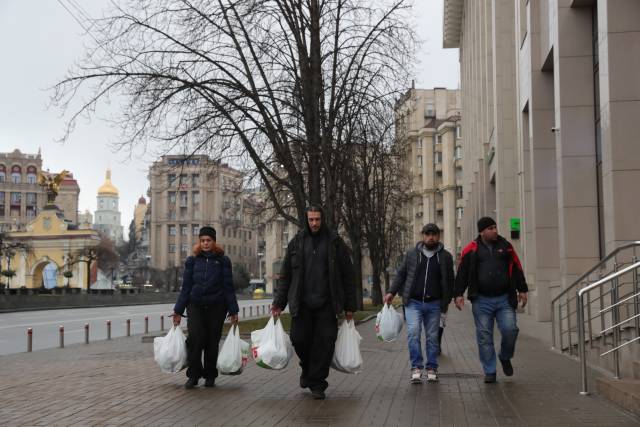 当地时间24日，在乌克兰基辅，当地居民拎着采购的物资走在街道上。 图源：新华社