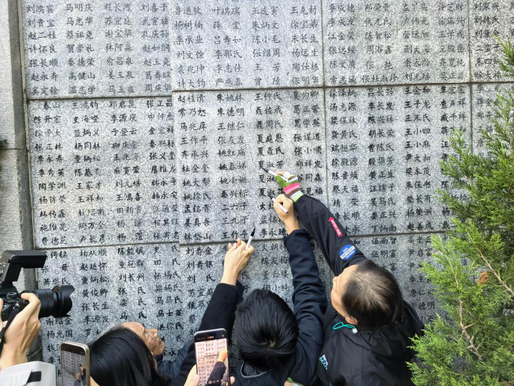 南京大屠杀幸存者夏淑琴指着“哭墙”上亲人的名字，女儿和曾外孙替她为亲人的名字“描新”。 新华社记者 邱冰清 摄