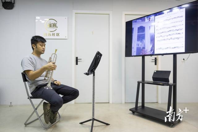 许宇翔认真听着屏幕中学生的吹奏。由于网络延时，他无法和学生合奏演练，只能轮流示范。
