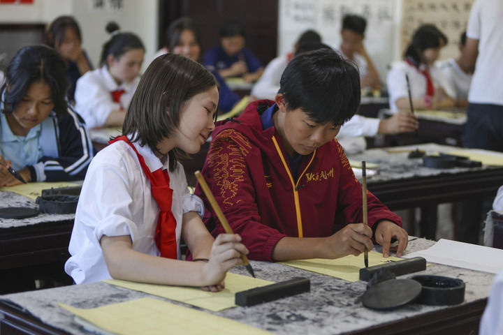 在新疆喀什地区疏附县托克扎克镇中心小学,来自贵州省黔西南布依族苗族自治州的青少年球员和小学生一起体验书法(2023年8月29日摄)。新华社记者 郝昭 摄