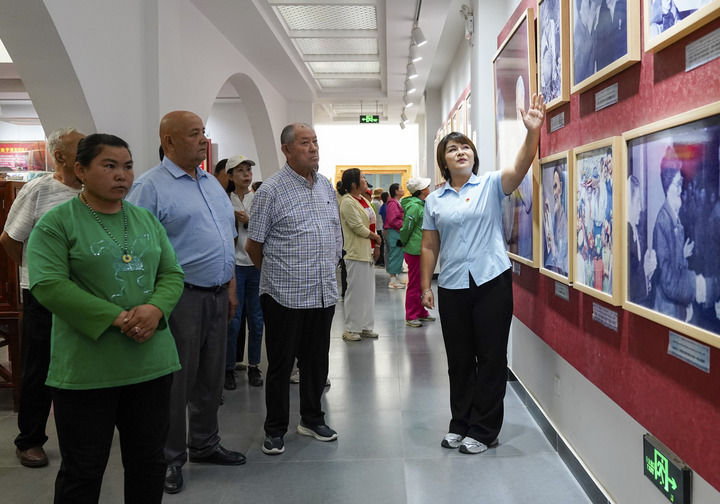 在新疆和田地区于田县库尔班·吐鲁木纪念馆,如克亚木·麦提赛地(右一)向参观者介绍展出的照片(2025年9月14日摄)。新华社记者 丁磊 摄