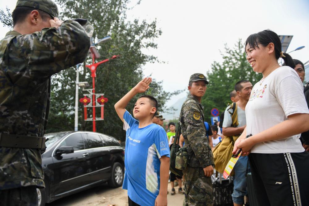 8月2日，在北京市门头沟区妙峰山镇，在乘坐车辆转移前，来自内蒙古的小学生武天骐（中）向武警北京总队机动第三支队的王雷鸣敬礼感谢。