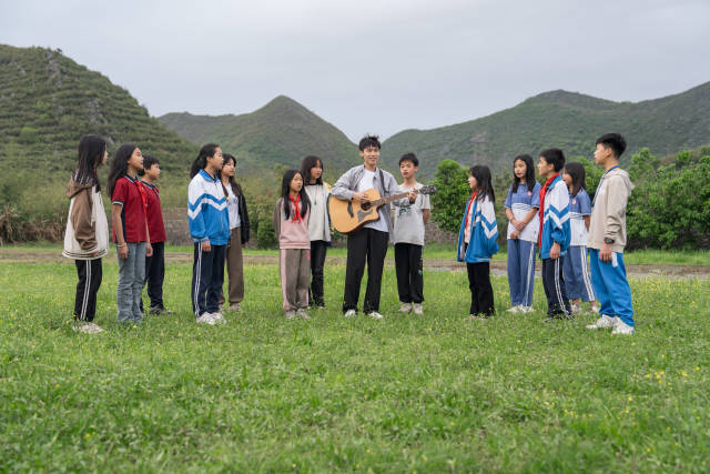 李鑫旺带领学生在红云中心学校的草地上唱歌，在山区孩子心里播下音乐的种子。