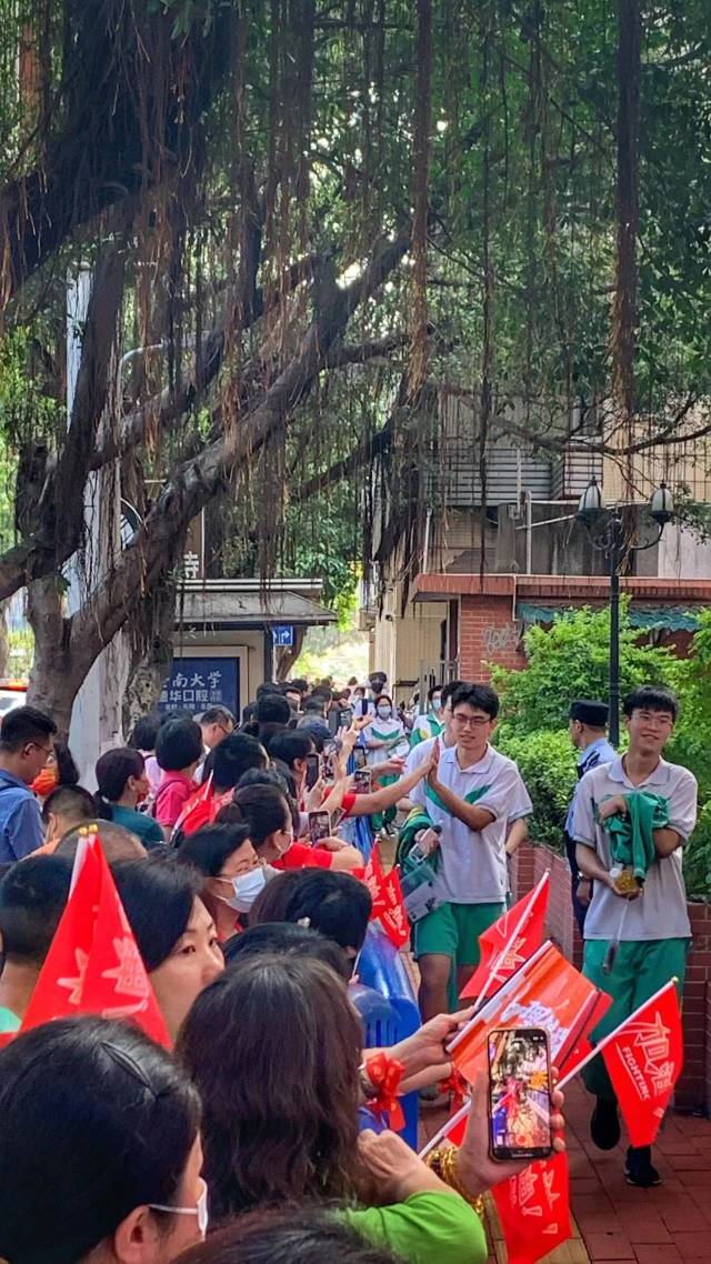 　　“跟昨天一样统一口号：南武加油，五班必胜！”6月8日上午8时，在广州市南武中学考点外，南武中学高三5班的十余位家长手持定制的小旗子、横幅，戴上红色腕带，与考生们击掌，为他们加油鼓劲。