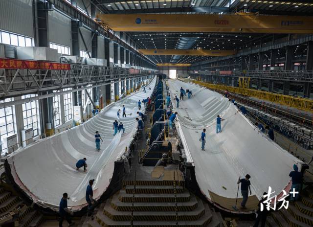 广东省汕尾明阳基地生产车间内，工人们正在对长达126米的风车叶扇内壁进行加固处理 