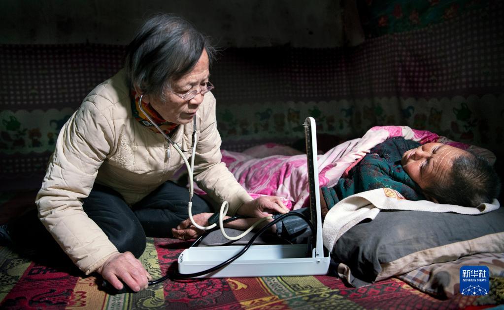 　　在陕西佳县店镇贺家沟村农家窑洞里，路生梅（左）跪坐在土炕上为瘫痪不起的村民乔爱芬义诊（2021年1月18日摄）。新华社记者 陶明 摄