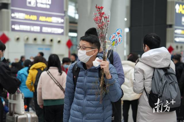 广州南站候车厅内，一位乘客举着腊梅去乘车。