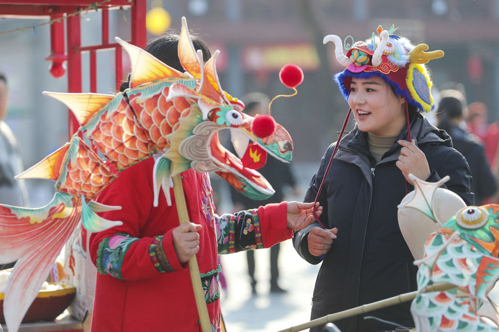  2024年2月13日，游客在河南商丘古城年货大集上购买龙帽。新华社发（李恒 摄）