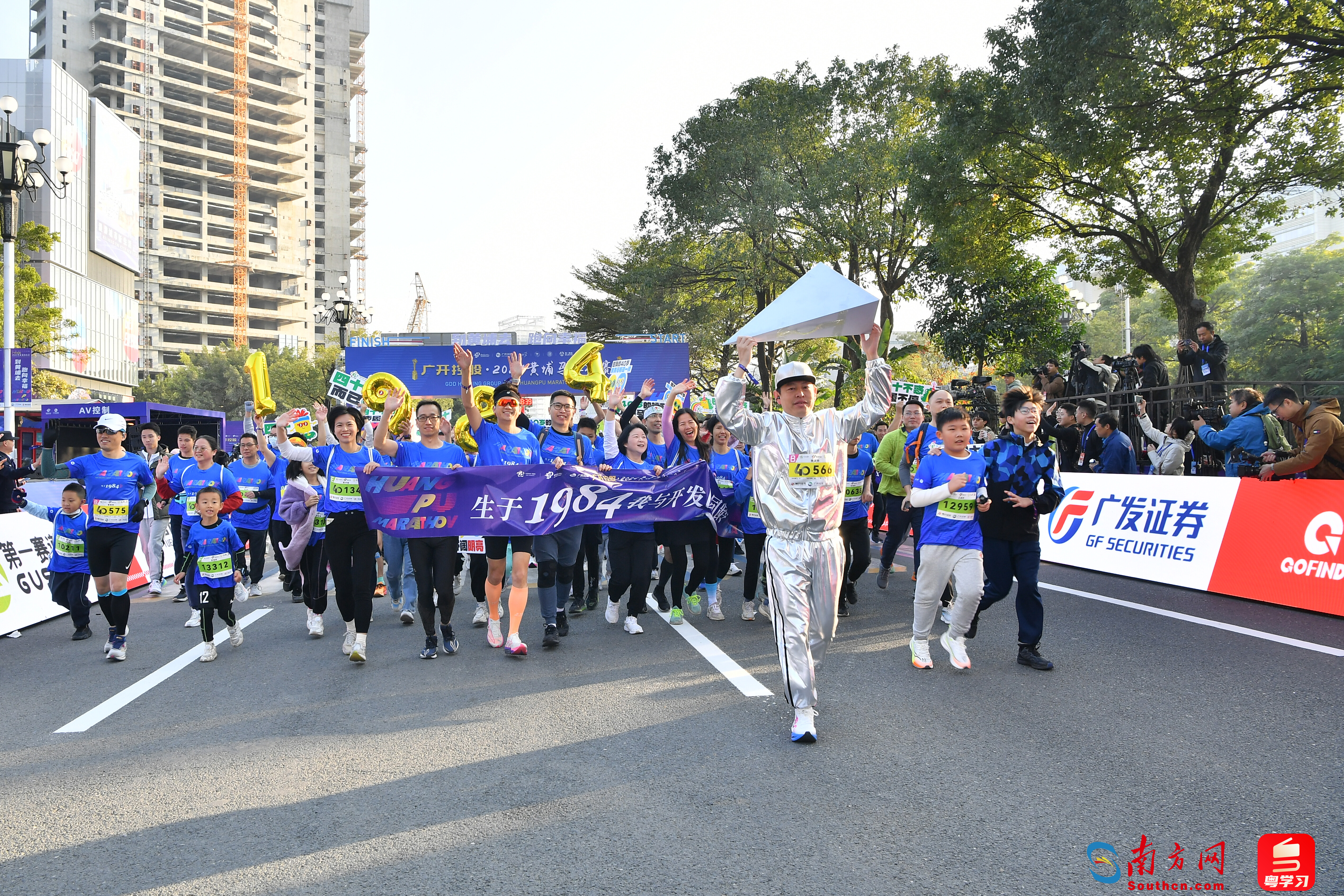 今年恰逢广州开发区建区40周年，40岁跑友组成“生于1984·我与开发区同龄”特色方阵亮相黄马赛道，领头的一名跑友身着银色衣服、手举立体三角形，模仿广州开发区标志性雕像“开拓者”。贾自豪 摄