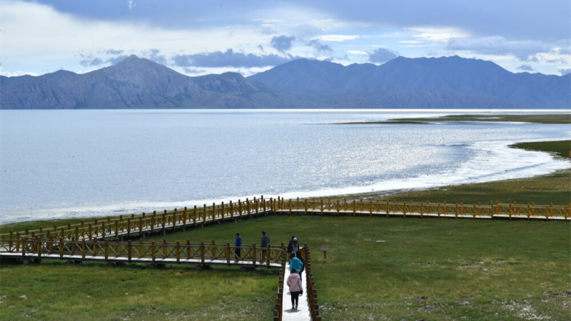 游客行走在青海玛多县冬格措纳湖畔的木栈道上。