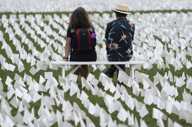 2021年9月17日，在美国首都华盛顿的华盛顿纪念碑附近的草坪上，参观者坐在白色旗帜中间，悼念美国超过66万名新冠逝者。新华社记者 刘杰 摄