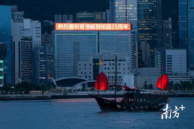 17/25 6月23日，香港维港两岸，多栋高楼亮灯庆祝香港回归祖国25周年，与海上帆船交相辉映。