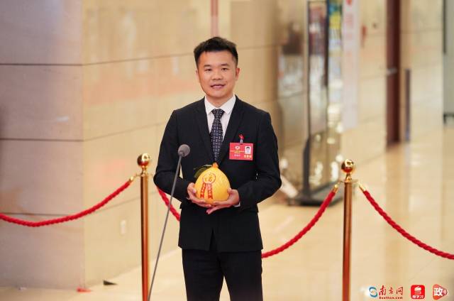 省政协委员、梅州市工商联副主席蔡雪峰手拿梅州金柚走上委员通道。