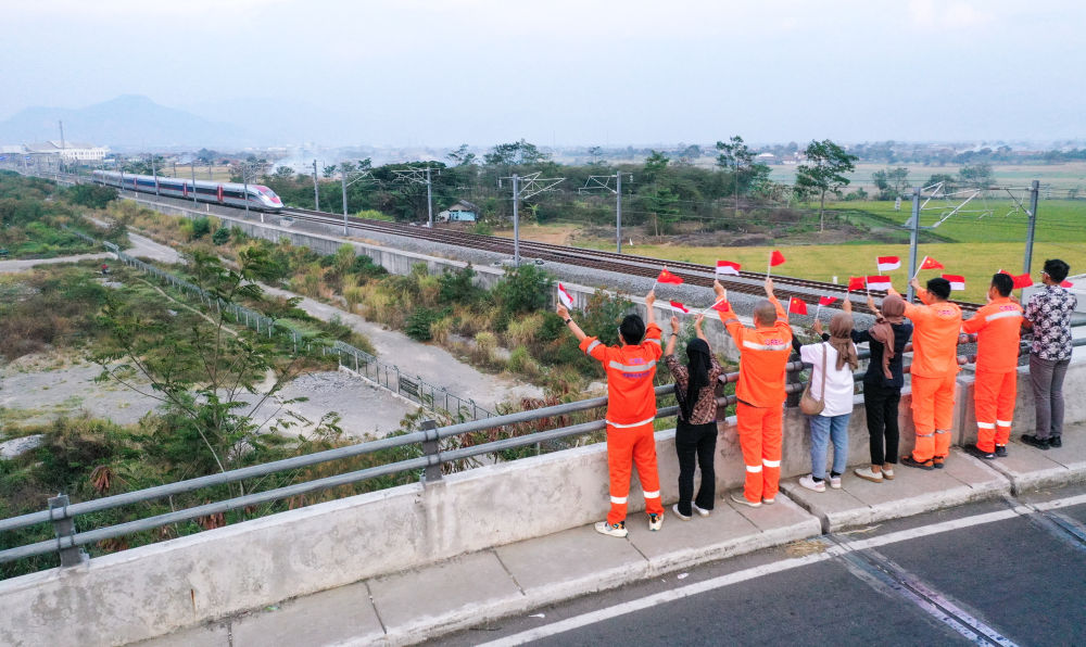 10月17日，在印度尼西亚万隆一座天桥上，雅万高铁建设单位之一中铁电气化局的中国和印尼籍员工挥舞着中国和印尼两国国旗，向远处驶来的一列雅万高铁高速动车组列车欢呼（无人机照片）。新华社记者 徐钦 摄